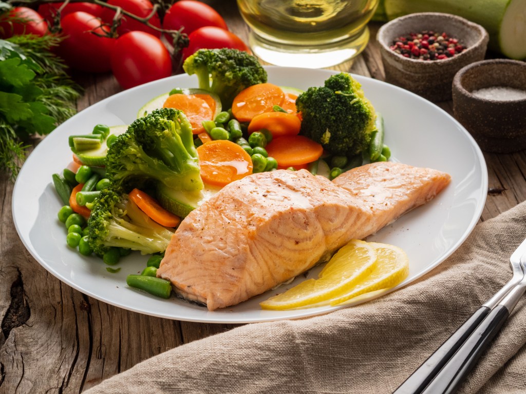 Steamed salmon and vegetables, paleo, keto, fodmap diet. White plate on old rustic wooden table, side view